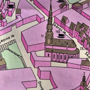 Op de afbeelding: Een kaartgedeelte in roze en beige, met gebouwen, straten en tekst. De kaart bevat de tekst "Skārņu ie" en nummers. Een kerk met een hoge toren is prominent aanwezig.