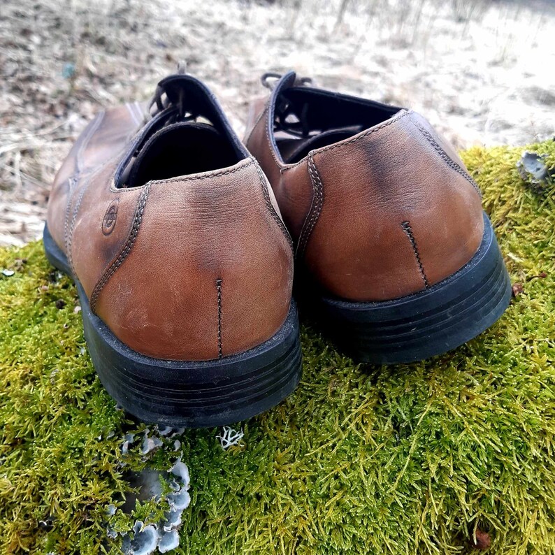 K&ouml;nnte beinhalten: Ein Paar braune Lederschuhe mit schwarzen Sohlen. Die Schuhe haben ein Schn&uuml;rdesign und sind getragen.