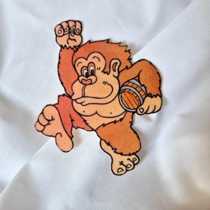 May include: A brown cartoon monkey with a barrel in its hand, running to the right. The monkey is wearing a brown loincloth and has a big smile on its face.