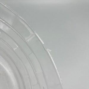 May include: Close-up of a clear plastic container with a slightly chipped edge. The container has a series of concentric rings around the edge.