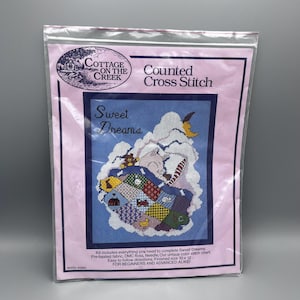 May include: A counted cross stitch kit featuring a sweet dreams design with a piglet sleeping under a patchwork quilt. The kit includes pre-basted fabric, DMC floss, a needle, and a color stitch chart. The finished size is 10 x 12 inches.  "For beginners and advanced alike!"