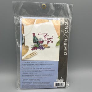 May include: A packaged cross-stitch kit for a wine-themed apron. The apron design features a wine bottle, a glass of wine, grapes, and the text "Conserve Water, Drink Wine". The kit includes instructions.