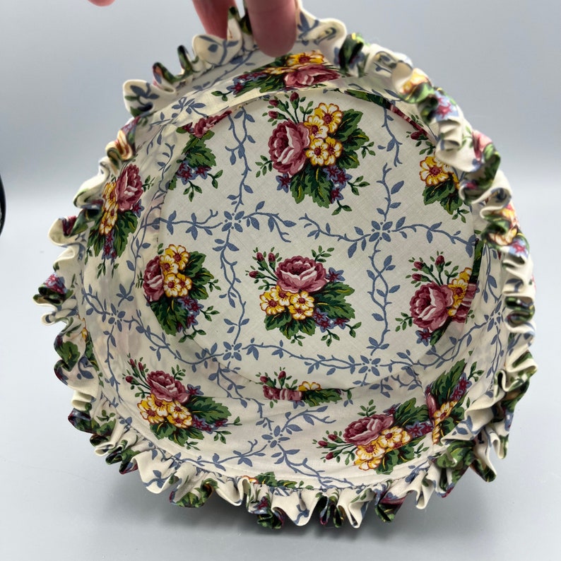 May include: A white fabric basket with a ruffled edge and a floral print featuring pink, yellow, and green roses on a white background with blue vines.