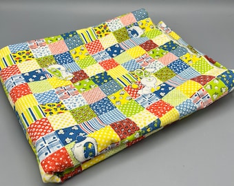 May include: A yellow, blue, red, and green patchwork fabric with a repeating pattern of small animals. The fabric is folded in half.