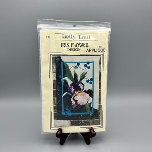 May include: A close-up of a quilting pattern for an iris flower applique. The pattern is on a white background with a picture of the finished applique in the center. The pattern is titled "Iris Flower Design to Applique" and is from Holly Trail.
