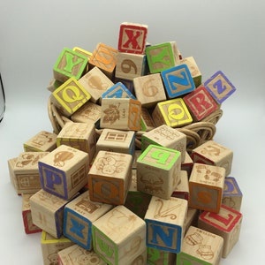May include: A pile of wooden alphabet blocks with various colors and letters, including Q, X, N, P, and Z. Some blocks have pictures of animals and objects, such as a leaf, an octopus, a pear, and a queen. The blocks are in a wicker basket.