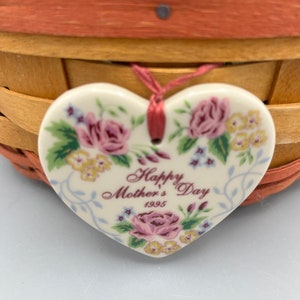 May include: A white ceramic heart-shaped ornament with a floral design and the text "Happy Mother's Day 1995".