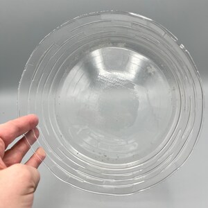 May include: A clear plastic pie plate with a raised rim and concentric circles. The plate is made by "Wilton", and has the text "Disposable Pie Plate" printed on the bottom.