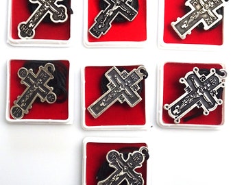 May include: Eight small, white boxes with red velvet interiors, each containing a silver-colored cross pendant with a black figure of Jesus Christ. The crosses have intricate designs and Cyrillic lettering.
