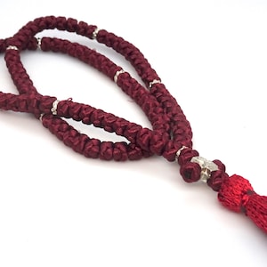 May include: A maroon prayer rope with silver beads and a red tassel. The rope is knotted and has a traditional design.
