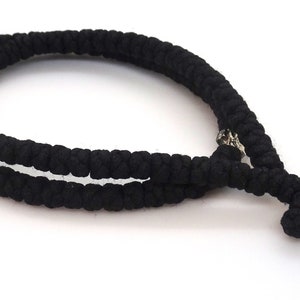 May include: Black knotted prayer rope with a silver cross charm. The rope is made of wool and has a traditional knot design.