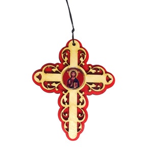 May include: A wooden cross with a red background and intricate gold detailing. The center of the cross features a round image of Jesus Christ.