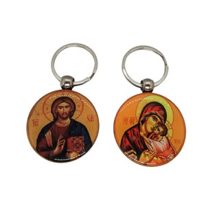 May include: Two silver keychains with round, colorful images. One keychain features a depiction of Jesus Christ holding a book, with the text "IC XC" on the image. The other keychain features a depiction of the Virgin Mary holding a baby Jesus, with the text "MP OY" on the image.