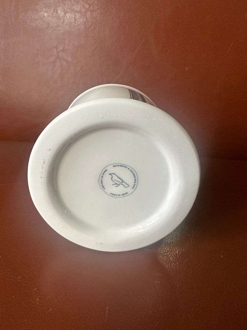 May include: White ceramic mug with a black and white bird design. The mug has a black rim and a black handle. The bottom of the mug has a black circle with the text "Made in China" and a bird design. The text "Microwave & Dishwasher Safe" is also printed on the bottom of the mug.