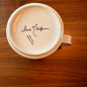 May include: White ceramic mug with a black signature that reads "Sara M. Halfmann" and the text "Made in China / Fabrique en Chine".