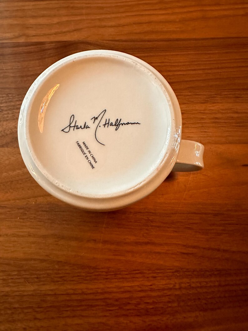 May include: White ceramic mug with a black signature that reads "Sara M. Halfmann" and the text "Made in China / Fabrique en Chine".