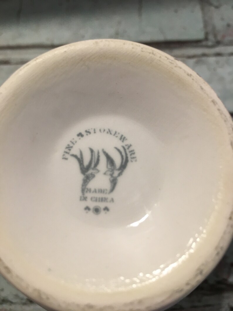 May include: Close-up of the bottom of a white ceramic mug with a blue and gray logo that reads "Fire Stoneware" and "Made in China".