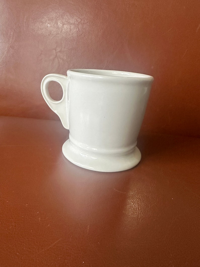 May include: White ceramic shaving mug with a handle and a wide base.