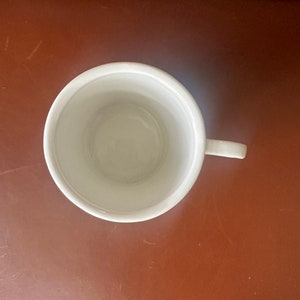 May include: A white ceramic mug with a handle. The mug is empty and has a smooth, glossy finish.