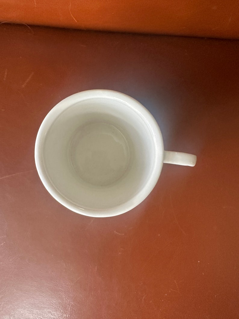 May include: A white ceramic mug with a handle. The mug is empty and has a smooth, glossy finish.