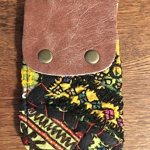 May include: A small green and yellow fabric pouch with a brown leather flap and two brass snaps. The pouch has a colorful embroidered design.