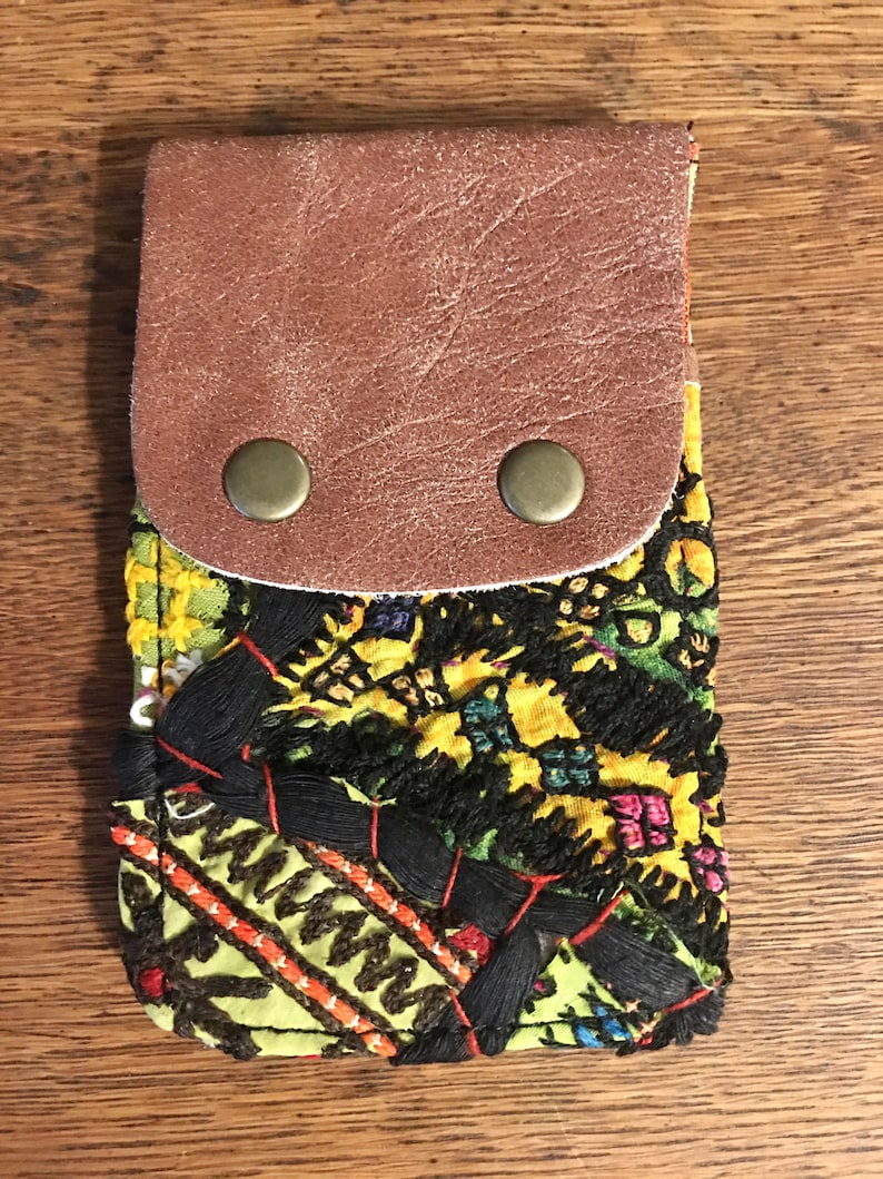 May include: A small green and yellow fabric pouch with a brown leather flap and two brass snaps. The pouch has a colorful embroidered design.