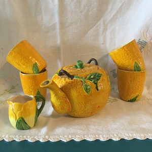 Puede incluir: Una tetera de cerámica amarilla y verde y cuatro tazas con forma de limones, con una jarra de crema a juego con forma de tulipán amarillo.