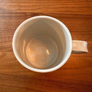 May include: A white ceramic mug with a rounded handle. The mug is empty and has a smooth, glossy finish.