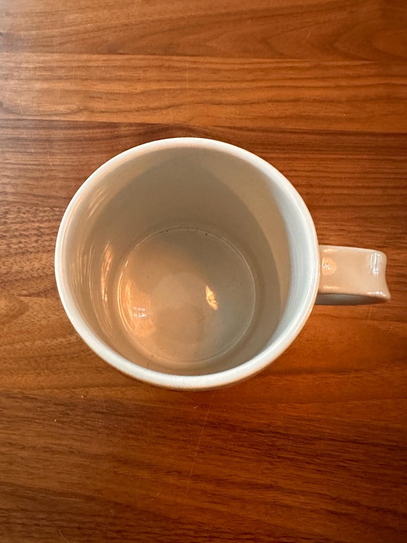 May include: A white ceramic mug with a rounded handle. The mug is empty and has a smooth, glossy finish.
