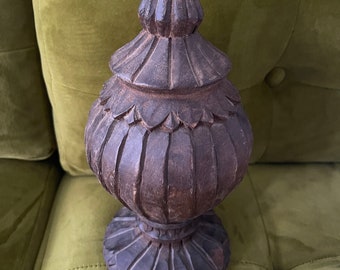 May include: A dark brown wooden finial with intricate carvings. The finial has a bulbous shape with a pointed top and a wide base.