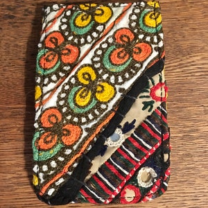 May include: A small, colorful, embroidered pouch with a patchwork design. The pouch is made of different fabrics and has a variety of colors, including red, orange, yellow, green, blue, and black.