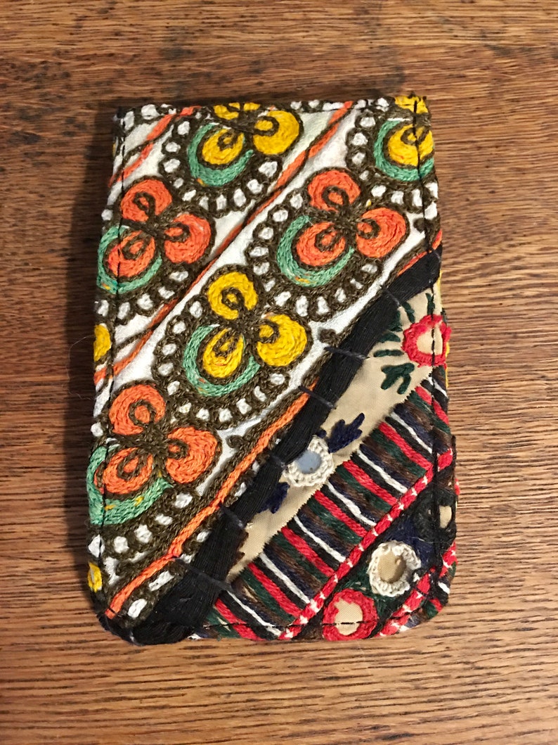 May include: A small, colorful, embroidered pouch with a patchwork design. The pouch is made of different fabrics and has a variety of colors, including red, orange, yellow, green, blue, and black.