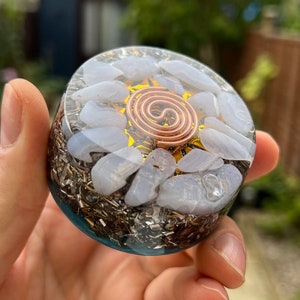 May include: A clear crystal orb with a copper wire spiral inside. The orb is filled with small white and gray stones. The orb is surrounded by a dark blue resin base.