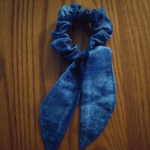 May include: A blue scrunchie with a bow. The scrunchie is made of a soft, silky fabric.