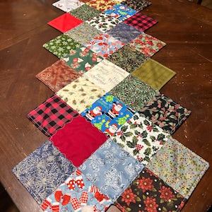 May include: A Christmas table runner made of patchwork fabric squares. The squares feature various holiday-themed patterns, including Santa Claus, holly, and snowflakes. The runner is a festive addition to any holiday table.