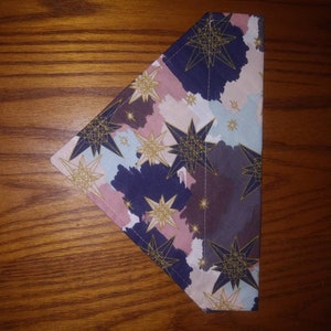 May include: A triangular fabric bandana with a geometric star pattern in gold on a background of pink, blue, and purple watercolour-like washes.