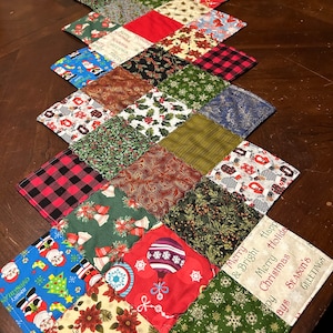 Puede incluir: Un camino de mesa de Navidad con un diseño de patchwork que presenta varios patrones navideños, incluyendo Papá Noel, adornos, campanas, copos de nieve y cuadros. El camino de mesa tiene un esquema de color rojo, verde, azul y blanco. El texto en el camino de mesa dice "Merry & Bright Happy Holidays Merry Christmas Happy Season's Greetings".