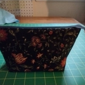 May include: A black zippered pouch with a floral print featuring red, pink, and gold flowers on a black background.