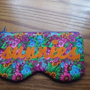 May include: A floral print zipped pouch with the word "sunnies" embroidered in orange thread.