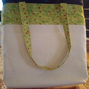 May include: A white canvas tote bag with green and yellow fabric straps featuring a bee and flower pattern.