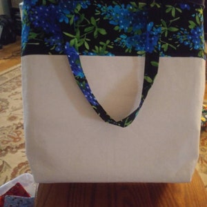May include: A white tote bag with black and blue floral fabric trim. The bag has two fabric handles.