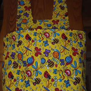 May include: Yellow tote bag with a colourful bug print featuring ladybugs, butterflies, dragonflies, bees, and snails. The bag has two straps.