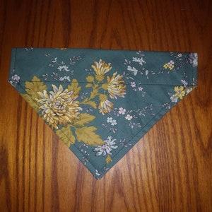 May include: A teal blue bandana with a floral pattern featuring yellow and white flowers. The bandana is folded in a triangular shape.