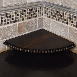 May include: A dark brown wooden corner shelf with a beaded edge. The shelf is mounted on a tiled wall.