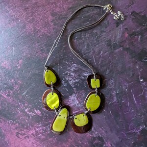 May include: A brown and green necklace with a cord and a silver clasp. The necklace features six large, irregularly shaped pendants with a green and brown marbled pattern.
