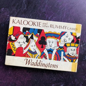 May include: A vintage game box for Kalooki and other Rummy games by Waddingtons. The box features colourful illustrations of playing card characters.
