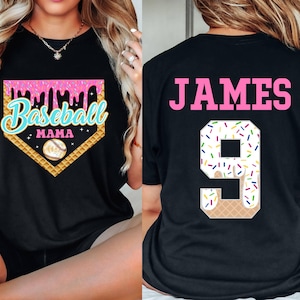 May include: Two black t-shirts. One shirt has a pink and blue baseball graphic with the text "Baseball Mama". The other shirt has the text "JAMES" in pink and a number "9" with a white and colorful sprinkle design.