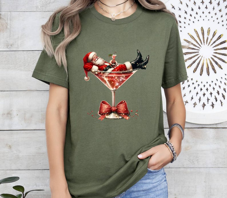 May include: A green t-shirt with a graphic of Santa Claus relaxing in a martini glass. The glass is decorated with a red bow and glitter.