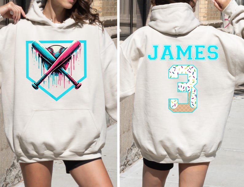 May include: Cream-colored hoodie with a baseball-themed graphic. The front features crossed bats and a baseball within a teal home plate shape. The back displays the name "JAMES" and the number "3" with a sprinkle and waffle cone design.