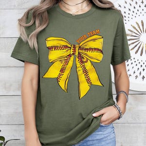 May include: A green t-shirt featuring a yellow softball bow and the text "Your Team" printed on the front.